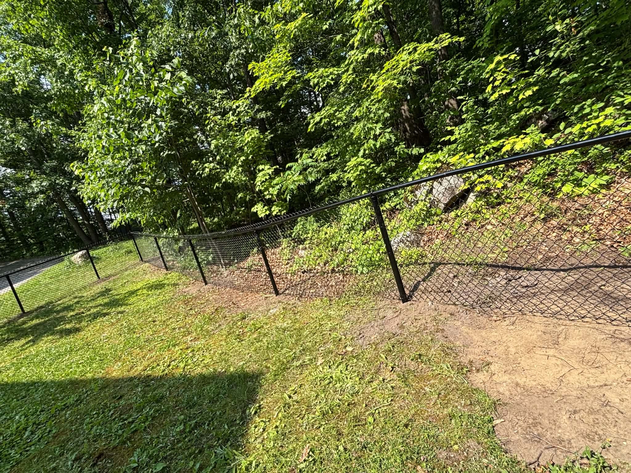 Clôture chaînée noire en terrain en pente boisé